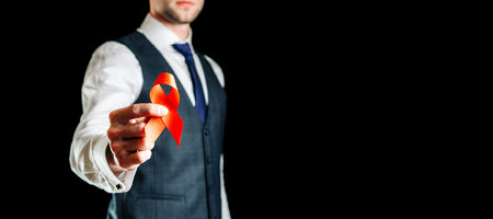 Hiv day. Red ribbon in hiv world day isolated on black background. Man holding awareness aids and cancer symbol. Aging Health month concept.の写真素材