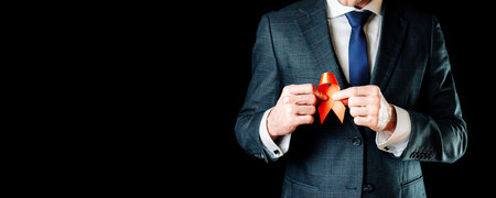 Aids hiv. Red ribbon symbol in hiv world day in man hand on black background. Awareness aids and cancer. HIV, AIDS and aging awareness month with copy spaceの写真素材