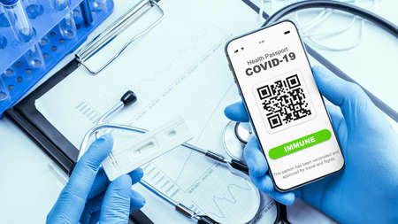 Coronavirus passport doctor holding. Covid vaccination certificate or vaccine passport on smartphone screen with doctor stethoscope, syringe and medical equipment on hospital white backgroundの写真素材