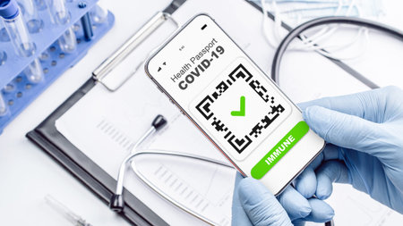 Coronavirus passport doctor holding. Covid vaccination certificate or vaccine passport on smartphone screen with doctor stethoscope, syringe and medical equipment on hospital white backgroundの写真素材