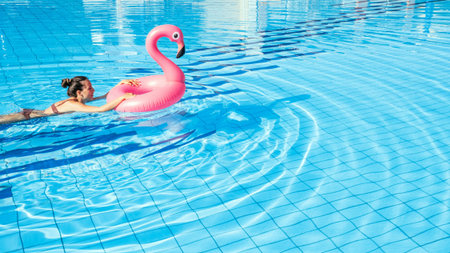 hello summer. Young sexy woman in bikini swimsuit with pink inflatable flamingo swimming in blue...