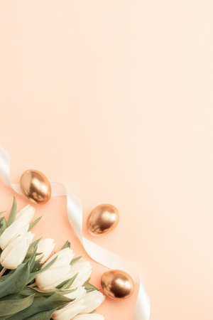 Golden eggs with spring white tulips on pastel pink background in Happy Easter decoration. Foil minimalist egg design, modern top view banner designの写真素材