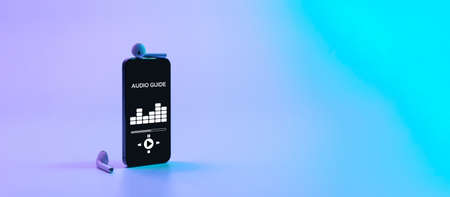 Audio guide online app on digital mobile smartphone screen with music headphones on neon background. Devices for listening audioguide to excursionsの写真素材