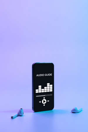 Audio excursion online app on digital mobile smartphone screen with music headphones on neon background. Listening audioguide. Education and leisure conceptの写真素材