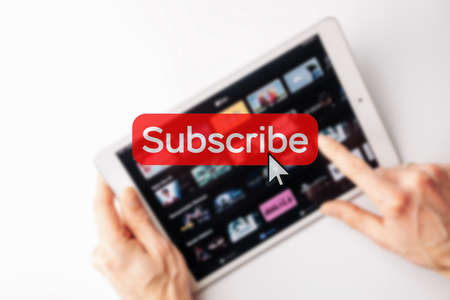 Subscribe now. Online video subscription red button. Internet service on laptop digital tablet blurred technology background. streaming video. communication networkの写真素材