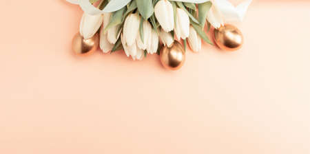 Golden eggs with spring white tulips on pastel pink background in Happy Easter decoration. Foil minimalist egg design, modern top view banner designの写真素材
