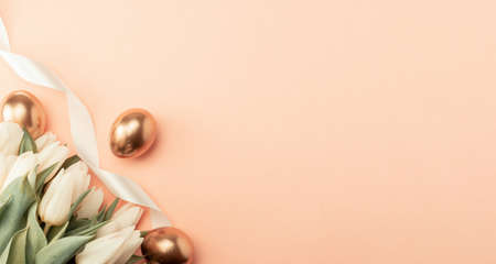 Golden eggs with spring white tulips on pastel pink background in Happy Easter decoration. Foil minimalist egg design, modern top view banner designの写真素材