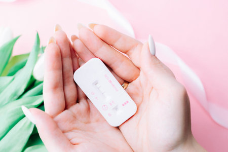 Pregnancy test couple. Positive woman pregnant test in hands with pink silk ribbon on tulips flower...