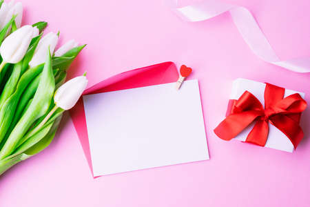 mother's day gift. Spring white tulip flower, gift with red ribbon on flat lay pink background. Valentines, birthday, women or wedding day conceptの写真素材