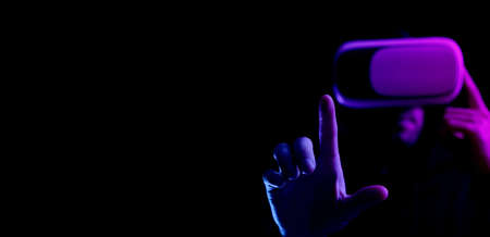 Vr helmet virtual reality. Model young in digital glasses for virtual reality technology isolated on dark neon background. Augmented reality, game, future technology concept. VRの写真素材