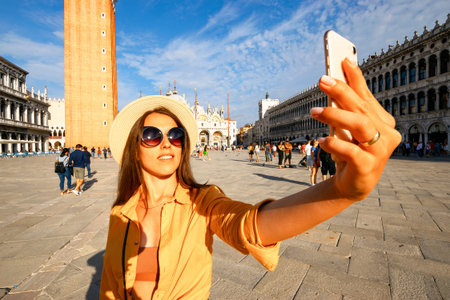 Travel blogger Venice Italy. Photographer girl with smartphone in Venice San Marco square. Paint building house in travel Europe Venezia city. Hispter tourist using her phone outdoorsの写真素材
