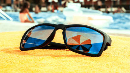 Sunglasses close up summer background. Beach pool equipment with travel sunglasses on yellow holiday towel. Outdoor relax holiday at oceanの写真素材
