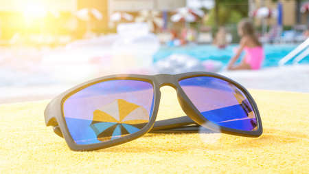 Sunglasses close up summer background. Beach pool equipment with travel sunglasses on yellow holiday towel. Outdoor relax holiday at oceanの写真素材