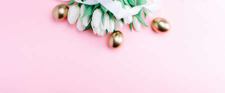 Golden eggs with spring white tulips on pastel pink background in Happy Easter decoration. Foil minimalist egg design, modern top view banner designの写真素材