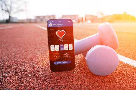fitness app. Smart phone screen with fitness health or sport gym mobile application on dumbbell background. App for training indoorsの写真素材