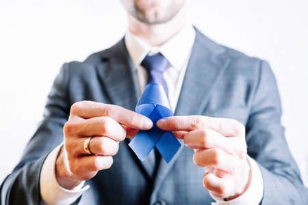 Blue ribbon cancer. Awareness prostate of health in November. Business man with blue ribbon in hands on white background. Symbol of oncology affected man. copy spaceの写真素材