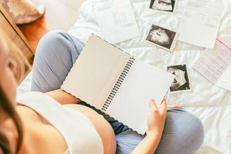 Baby list pregnant woman. Young pregnancy mother holding notepad. Pregnant lady writing check list of baby. Concept of maternity, expectation.の写真素材