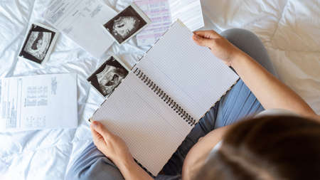 Baby list pregnant women. Young pregnancy mother holding notepad. Pregnant lady writing check list of baby. Concept of maternity, expectationの写真素材