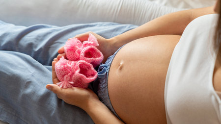 Pregnancy baby shoes. Happy pregnant woman holding pink baby shoes. Small child shoe. Concept of...