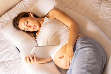 Pregnant tablet health app. Pregnant woman holding digital tablet. Mobile pregnancy online maternity application. Concept of pregnancy, maternity, expectation for baby birthの写真素材