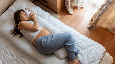 Pregnant sleeping pillow woman. Young pregnancy mother sleep with pregnant belly support pillow. Concept of pregnancy, maternity, expectation for baby birthの写真素材