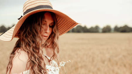 Beauty romantic girl outdoors. Happy young woman in sun hat in summer wheat field at sunset. Copy space, sunset, flare light, summer season. Boho chic styleの写真素材