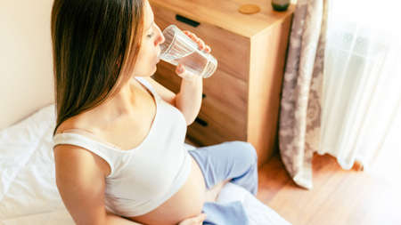 Pregnant drinking water. Young pregnancy mother drink water. Pregnant lady waiting of baby. glass of water. Concept maternity, childbirthの写真素材