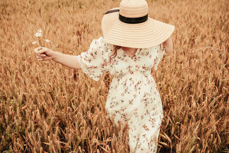 Hand wheat field woman. Happy young woman in sun hat in summer wheat field at sunset. Nature, summer holidays, agriculture and people conceptの写真素材
