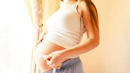 Belly size pregnancy woman measure. Happy young pregnant woman with tape measuring belly. Therapy, healthcare, motherhood conceptの写真素材