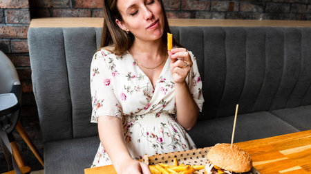 Hungry pretty pregnancy female eating tasty burger. Fast food, people and unhealthy eating conceptの写真素材