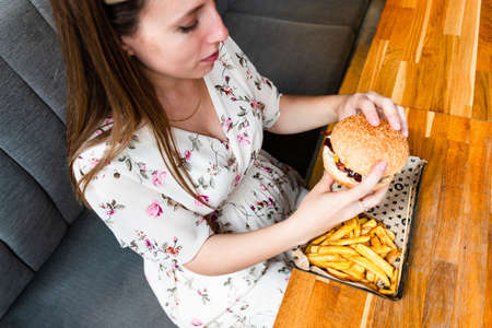 Burger pregnant girl eat. Hungry happy pregnancy woman eating tasty hamburger. Junk food conceptの写真素材