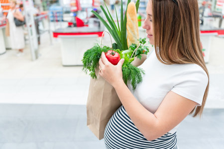 Pregnant healthy food bag. Pregnancy woman with healthy vegetables fresh, lettuce salad leaves in market food bag on grocery supermarket background. healthy food backgroundの写真素材