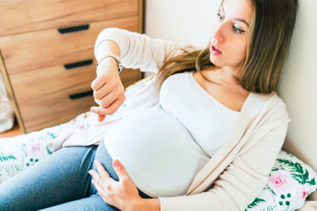 Pregnant pain contractions. Pregnant woman watching clock, holding baby belly. Childbirth time, contractions pain. Pregnancy, medical health care conceptの写真素材