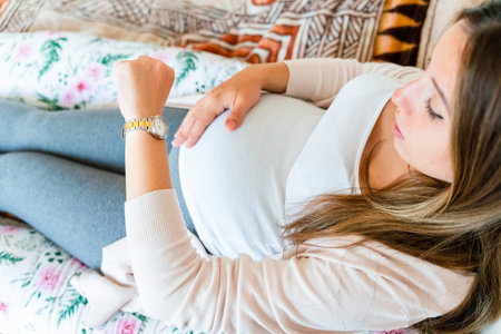 Pregnant clock time childbirth. Childbirth time, contractions pain. Pregnancy woman watching clock, holding baby belly. Pregnancy, medical health care conceptの写真素材