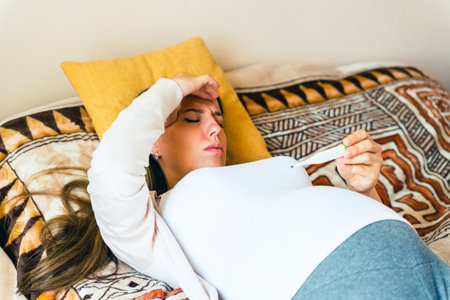 Pregnancy health temperature check. Pregnant woman holding thermometer, check fever flu temperature. Pregnancy girl sick. Concept maternity, pregnant, childbirthの写真素材