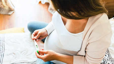 Pregnancy flu thermometer. Pregnant woman holding thermometer, check fever flu temperature. Pregnancy girl sick. Therapy, healthcare, motherhood conceptの写真素材
