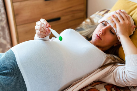 Pregnancy health temperature check. Pregnant woman holding thermometer, check fever flu temperature. Pregnancy girl sick. Concept maternity, pregnant, childbirthの写真素材