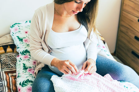 Knitting baby winter clothes. Cute pregnant woman knit fashion winter baby girl clothes. Pregnancy mother crochet kid cloth. Warm winter cozy clothes for babyの写真素材