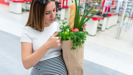 Woman supermarket grocery bag. Pregnancy mother with healthy vegetables, fresh lettuce salad leaves in market food bag on grocery supermarket background. Everyday shopping conceptの写真素材