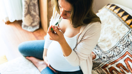 Pregnancy fever temperature check. Pregnant woman holding thermometer, check fever flu temperature. Pregnancy girl sick. Concept maternity, pregnant, childbirthの写真素材