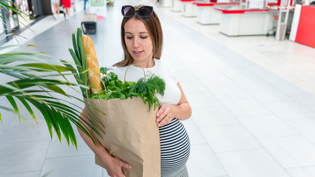 Woman supermarket grocery bag. Pregnancy mother with healthy vegetables, fresh lettuce salad leaves in market food bag on grocery supermarket background. Everyday shopping conceptの写真素材