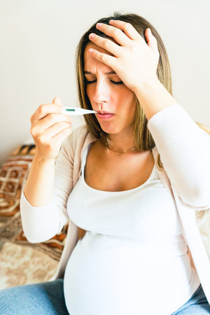 Pregnant headache fever sick. Pregnancy woman holding thermometer, check fever flu temperature. Pregnant girl sick. Pregnancy, medicine health care concept.の写真素材