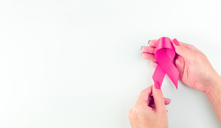 Pink ribbon banner. Woman hands holding health care symbol pink ribbon on white background. Breast cancer support with copy space.の写真素材