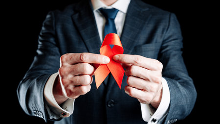 Hiv aids. Red ribbon in hiv world day isolated on dark background. Man holding awareness aids and cancer symbol. Health, Medical sign. copy space.の写真素材