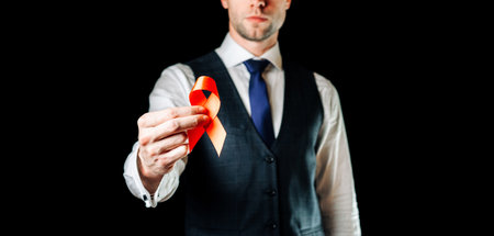 hiv aids. Red ribbon in hiv world day isolated on dark background. Man holding awareness aids and cancer symbol. Health, medical sign. copy spaceの写真素材