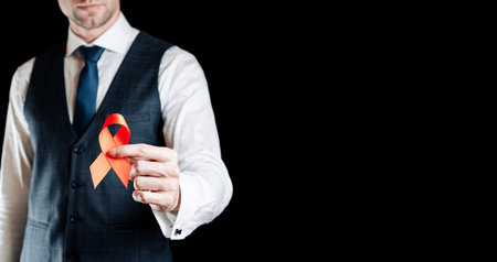 hiv day. Red ribbon in hiv world day isolated on black background. Man holding awareness aids and cancer symbol. Aging health month conceptの写真素材