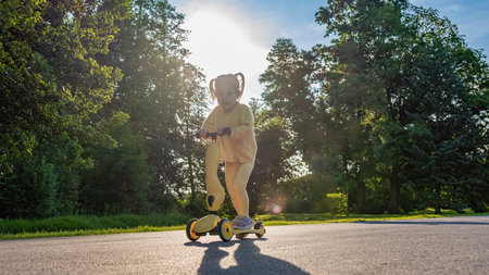 Little girl scooter. Toddler riding yellow scooter. Park road summer play.