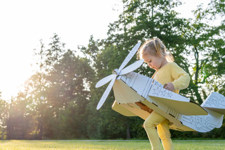 Cardboard pilot. Girl dress-up play child. Park dream aviation outdoor.
