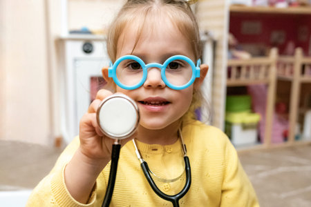 Toddler girl open mouth laugh stethoscope glasses raised handの写真素材