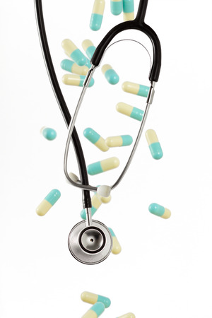 Phonendoscope on the background of falling down pills. Isolated on white backgroundの写真素材